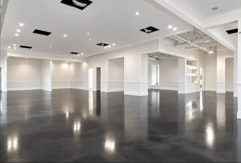 Grand espace commercial terminé au plancher époxy métallisé gris, lustré et réfléchissant, qui renvoie l’éclairage et les murs blancs moulurés