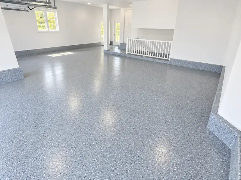 Garage résidentiel lumineux fini en époxy à flocons gris, flocons remontés sur la plinthe et la marche